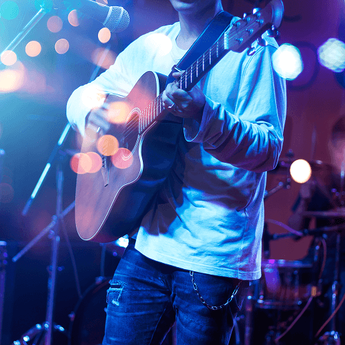 A musician playing an acoustic guitar on stage under blue and purple concert lights.