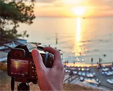 photographer and camera capturing sunrise over water